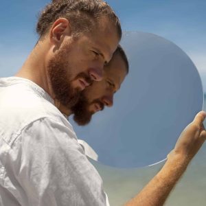 man-beach-posing-with-round-reflective-mirror-scaled.jpg